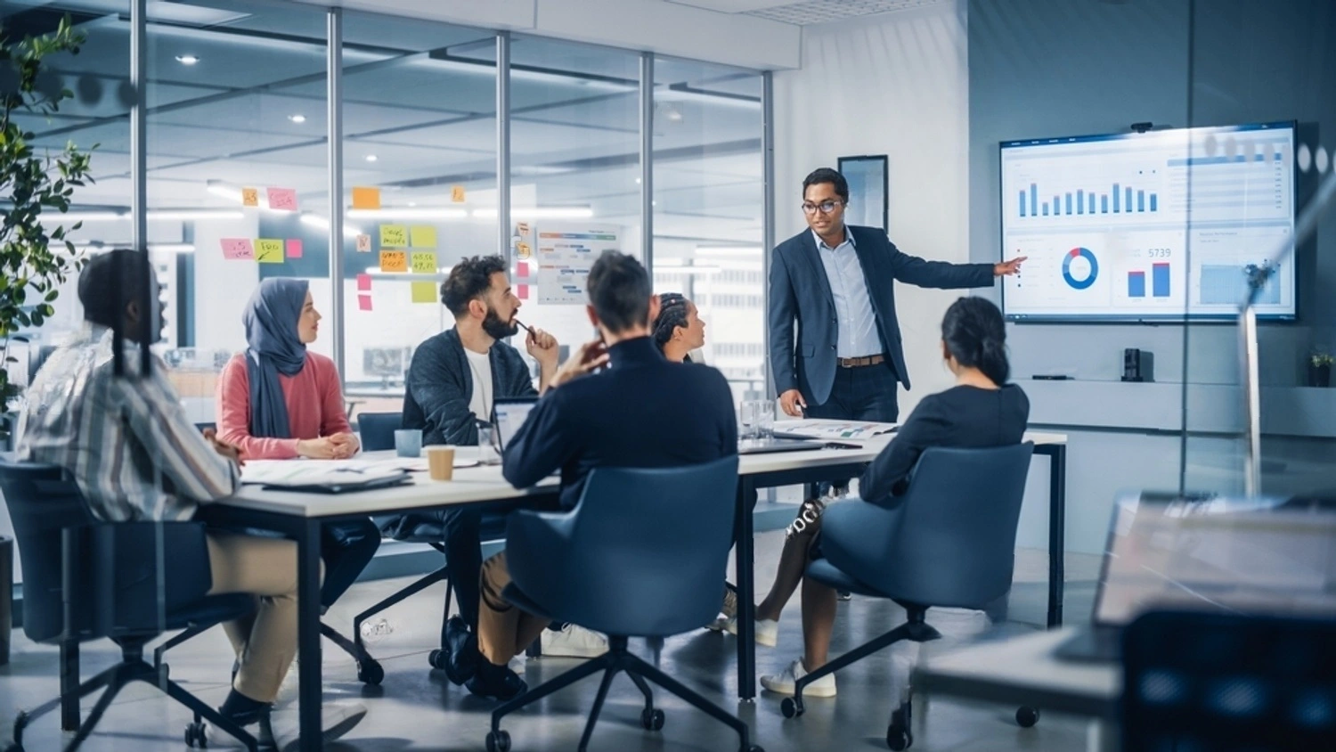 Várias pessoas em uma mesa de reunião analisando um gráfico financeiro em uma televisão